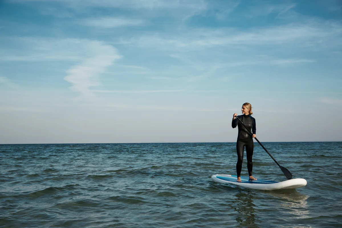Frau im Neoprenanzug beim Stand Up Paddeln auf ruhigem Wasser