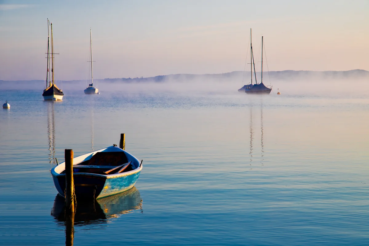 Ruderboot und Segelboote im Morgennebel auf einem ruhigen Voralpensee